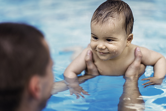 Father holding a smiling baby in a swimming pool