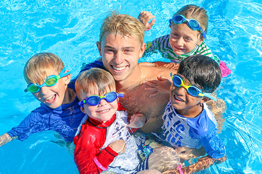 Four young kids in a swimming pool with their swim instructor for water safety