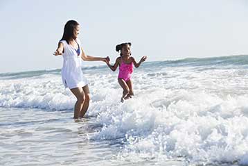 Woman holding a child's hand as they wade in the water at the beach